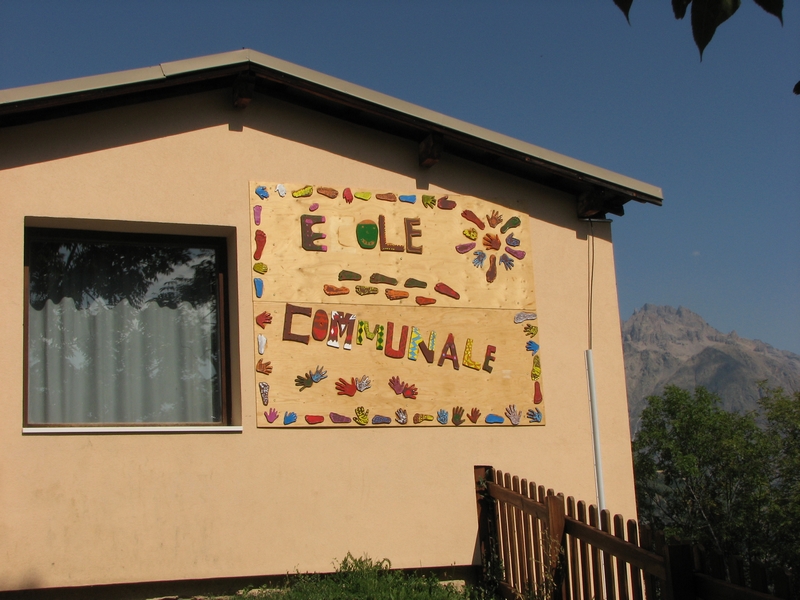 Les pieds et les mains des enfants encadrent et se promènent parmi les lettres ECOLE COMMUNALE.