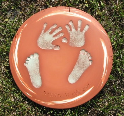 Plaque ronde dcore avec des liserets de porcelaine sur le pourtour supportant en son centre les empreintes (mains et pieds) d'un bb.